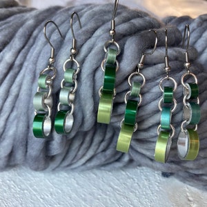 May include: Several pairs of handmade earrings with a chain link design. The earrings feature a combination of silver-tone metal and green, light green, and teal colored links. The earrings are displayed on a gray, textured surface.