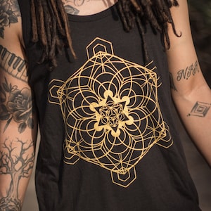 May include: A black tank top with a gold geometric design. The design is a complex pattern of circles and lines, creating a mandala-like effect.