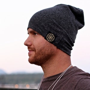 Puede incluir: Un gorro de lana gris oscuro con un peque&ntilde;o parche negro que presenta un dise&ntilde;o geom&eacute;trico dorado.