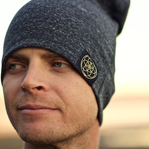 Puede incluir: Un gorro gris con un parche negro que presenta un dise&ntilde;o geom&eacute;trico dorado. El gorro est&aacute; hecho de un material suave y c&oacute;modo.
