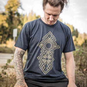 May include: A navy blue t-shirt with a gold geometric design. The design features a mandala-like pattern with a black center.
