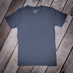 May include: A plain dark gray t-shirt with a small logo on the front that says "Sacred State".