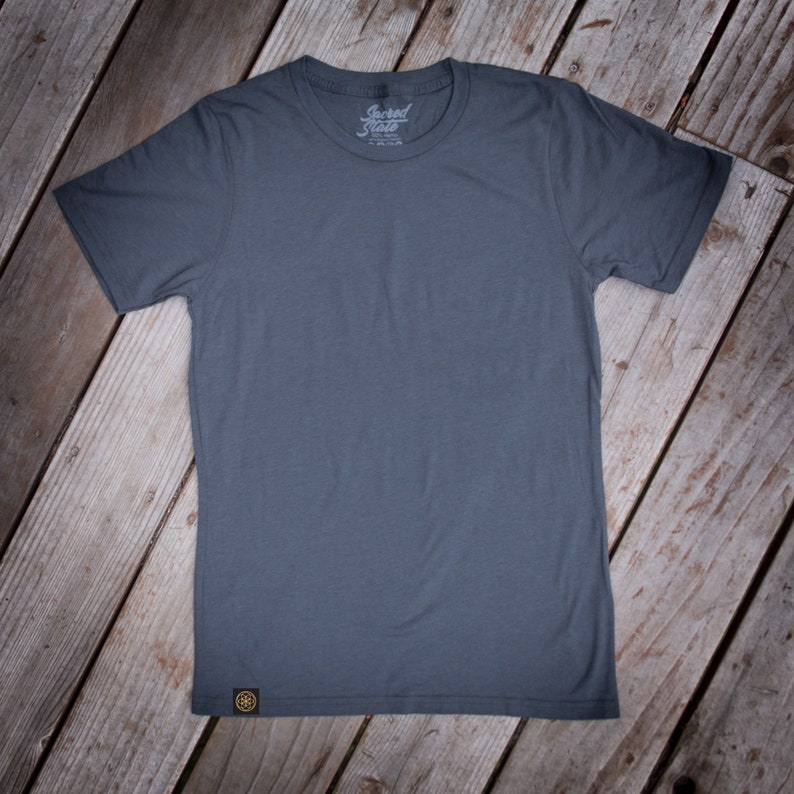 May include: A plain dark gray t-shirt with a small logo on the front that says "Sacred State".
