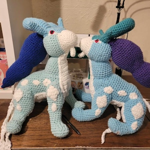 Könnte beinhalten: Zwei gehäkelte Plüschtiere, eines blau und weiß mit einem blauen Schwanz und das andere blau und weiß mit einem lila Schwanz.