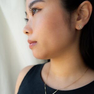 May include: A woman wearing a black tank top with a gold necklace and earrings. The necklace and earrings feature a delicate flower design.