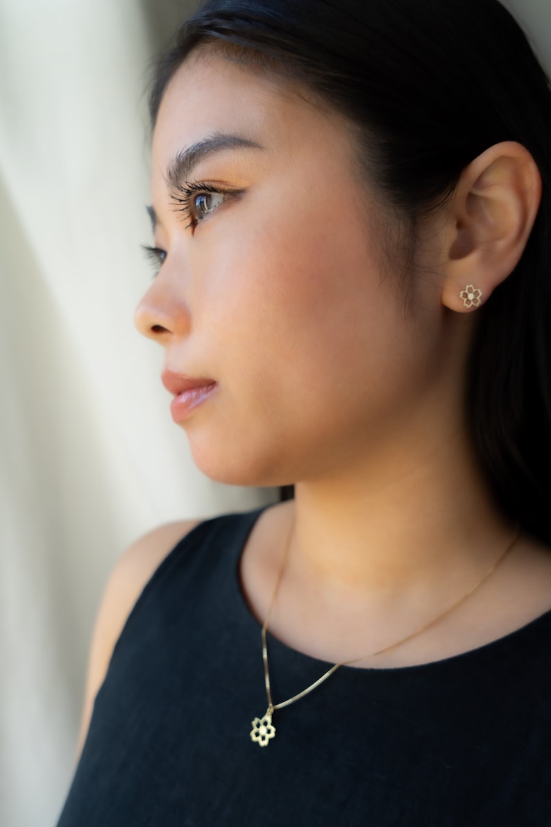 May include: A woman wearing a black tank top with a gold necklace and earrings. The necklace and earrings feature a delicate flower design.