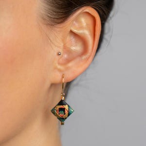 May include: Gold dangle earrings with a black, green, and orange geometric patterned charm.
