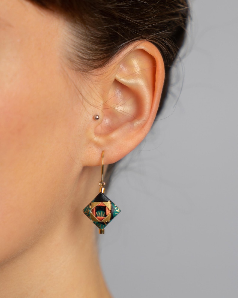 May include: Gold dangle earrings with a black, green, and orange geometric patterned charm.