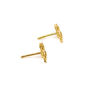 May include: A pair of gold-coloured stud earrings. Each earring has a delicate, openwork floral design. The earrings are set against a clean white background, highlighting their intricate details and polished finish.