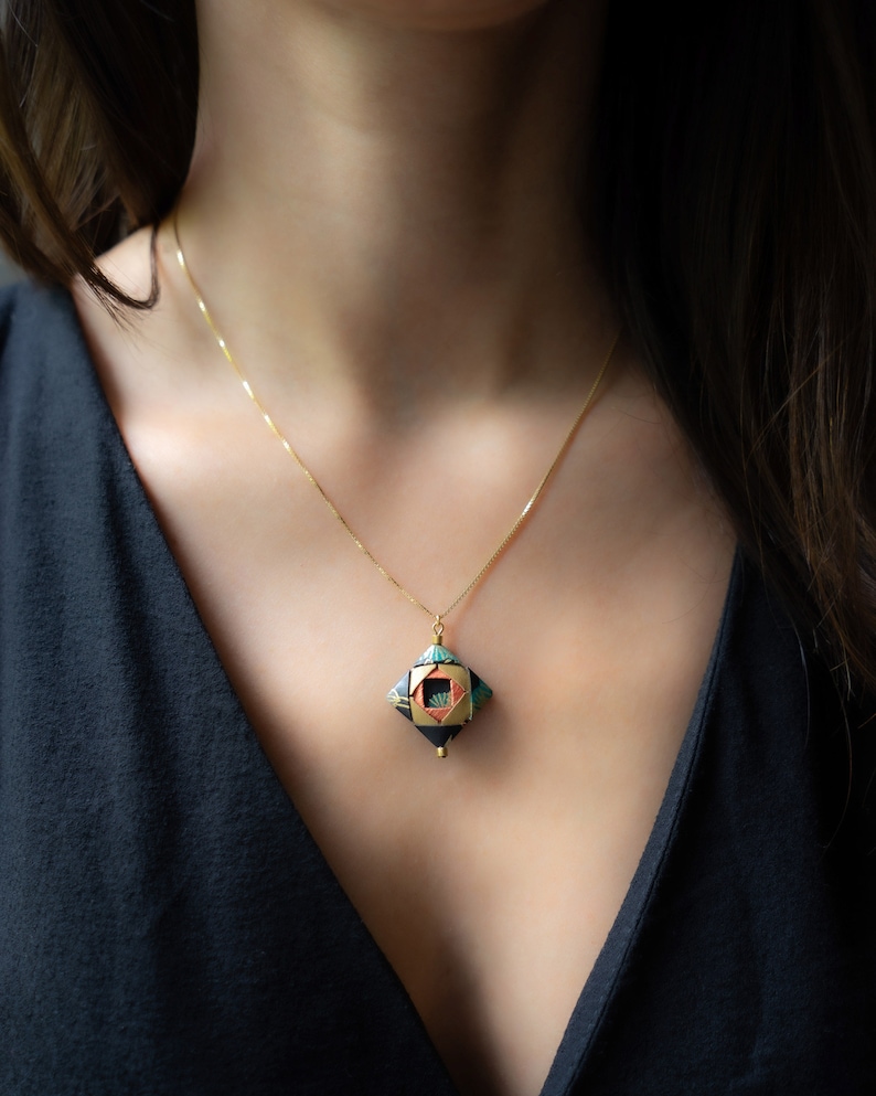 May include: A gold chain necklace with a geometric pendant. The pendant is black with green, orange, and gold accents.