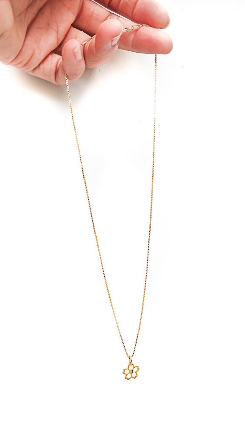 May include: A gold chain necklace with a delicate flower pendant.