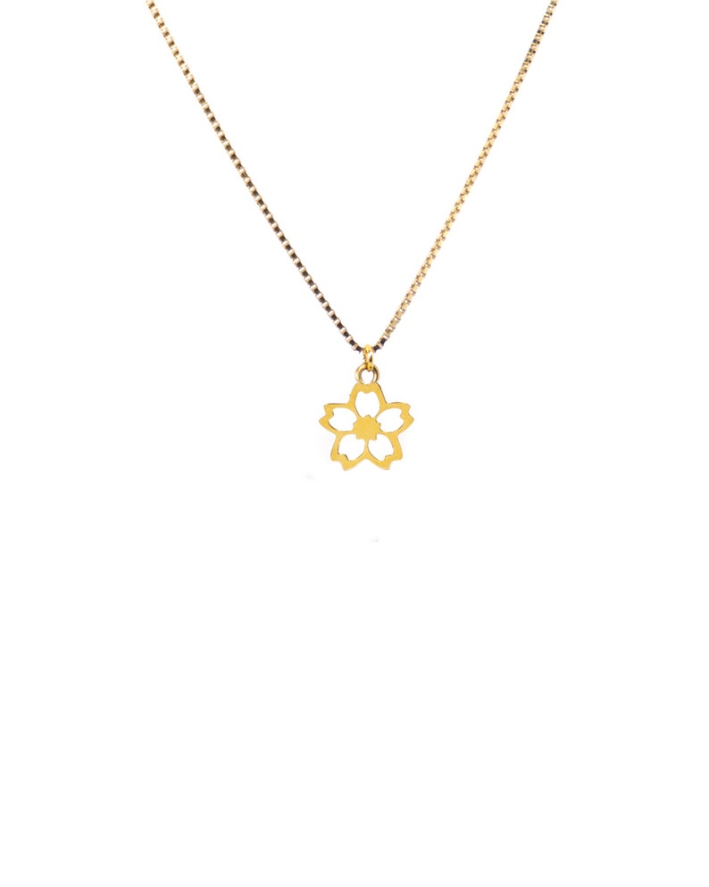 May include: A gold necklace featuring a fine chain and a floral pendant. The pendant is a five-petaled flower design. The necklace is shown against a plain white backdrop.
