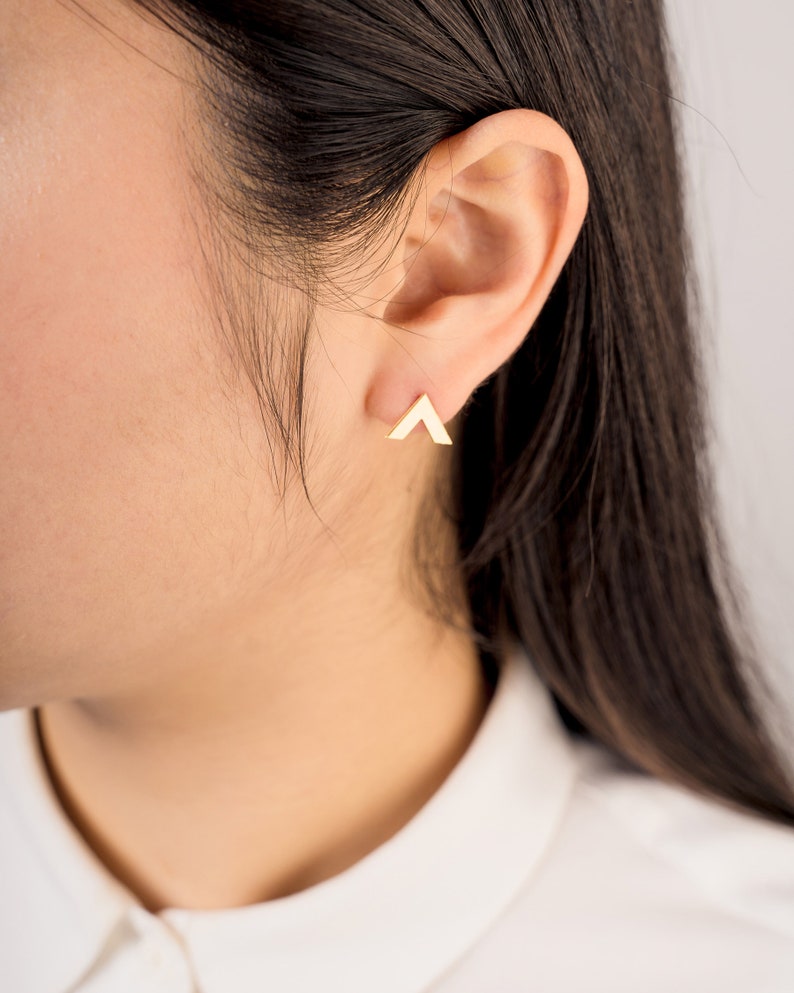 May include: A pair of gold triangle stud earrings. The earrings are small and simple, and they are a great way to add a touch of style to any outfit.