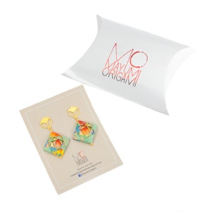 May include: A pair of origami earrings with a geometric design. The earrings are made of colorful paper and have gold accents. The earrings are packaged in a white pillow box with the brand name "Mayumi Origami" printed on it.