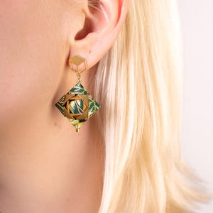 May include: Gold geometric earrings with a green and gold patterned design. The earrings are dangling and have a square shape.