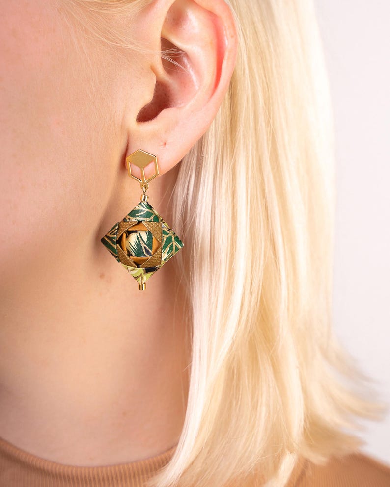 May include: Gold geometric earrings with a green and gold patterned design. The earrings are dangling and have a square shape.