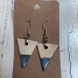 May include: A pair of ceramic triangle earrings with a white glaze and blue and brown accents. The earrings have silver hooks.