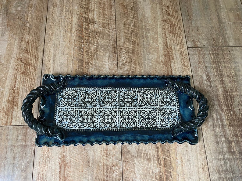 May include: Rectangular ceramic serving tray with a dark blue border and handles. The center features a white and black patterned design. The tray has a scalloped edge and is placed on a wooden surface.