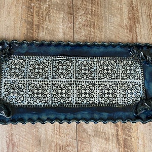 May include: Rectangular ceramic serving tray with a dark blue glaze and a decorative white and black tile pattern. The tray has a wavy edge and twisted rope handles, perfect for serving appetizers or desserts.