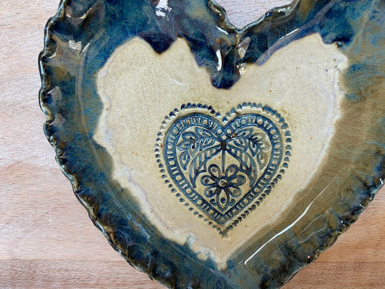 Puede incluir: Un plato de cer&aacute;mica en forma de coraz&oacute;n con un esmalte azul y un interior blanco. El plato tiene un dise&ntilde;o de coraz&oacute;n en relieve en el centro con un patr&oacute;n floral.
