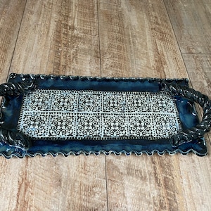 May include: Rectangular ceramic serving tray with a dark blue glaze and a decorative black and white tile pattern. The tray has twisted rope-style handles and a scalloped edge. A decorative piece for serving.
