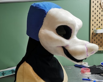 May include: A white foam fursuit head with a blue fabric lining and a black fabric neck piece. The head is on a foam base and is being worked on. The text "Fursuit Head Lining Tutorial" is visible at the top of the image.