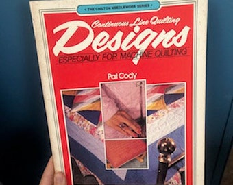 May include: A book titled "Continuous Line Quilting Designs - Especially for Machine Quilting" by Pat Cody. The book cover features a colorful quilt design with a red, white, and blue color scheme.