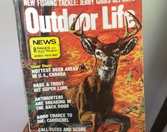 May include: A vintage copy of Outdoor Life magazine featuring a cover image of a white-tailed deer in a forest setting. The magazine cover text includes "NEWS", "HOTTEST DEER AREAS IN U.S., CANADA", "BASS & TROUT HIT SUPER LURE", "ANTIHUNTERS ARE SNEAKING IN THE BACK DOOR", "GOOD CHANCE TO DIE: CARMICHEL", "CALL DUCKS AND SCORE", and "NOSTALGIA-AIN'T NO".