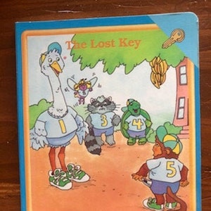 May include: A children's book titled "The Lost Key" featuring colorful illustrations of animals wearing numbers on their shirts. The animals include an ostrich, a raccoon, a turtle, and a monkey.