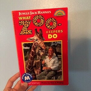 May include: A red book titled "What Zoo Keepers Do" by Jungle Jack Hanna. The book features a photo of a giraffe and a man in a zoo setting. The book is part of the Scholastic Reading Counts program.