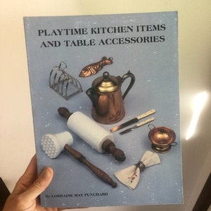 May include: A book titled "Playtime Kitchen Items and Table Accessories" by Lorraine May Punchard. The book cover features a variety of miniature kitchen items, including a rolling pin, a tea kettle, a fish-shaped cookie cutter, a strainer, and a napkin.