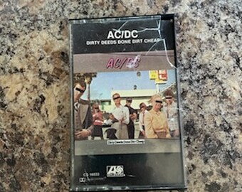 May include: A black cassette tape with a picture of a band on the front. The band is AC/DC and the album is "Dirty Deeds Done Dirt Cheap".