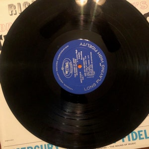 K&ouml;nnte beinhalten: Eine schwarze Schallplatte mit einem blauen Etikett, auf dem "Long Playing High Fidelity" und "The Sound of Music" steht, mit dem K&uuml;nstler Richard Hayman und seinem Orchester. Die Schallplatte befindet sich auf einem wei&szlig;en Hintergrund mit dem Text "Mercury Records Corporation" und "MGW 12228".