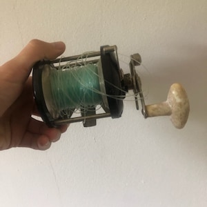 May include: A vintage fishing reel with a black body, a silver handle, and a green fishing line wound around the spool.