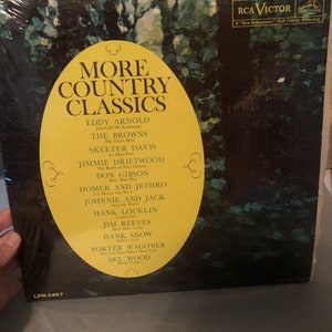 May include: A vintage vinyl record album cover with a yellow and black design. The album title is "More Country Classics" and features a list of country music artists and songs, including Eddy Arnold, The Browns, Skeeter Davis, Jimmie Driftwood, Don Gibson, Homer and Jethro, Johnnie and Jack, Hank Locklin, Jim Reeves, Hank Snow, Porter Wagoner, and Del Wood. The album is on the RCA Victor label.