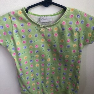 May include: A green baby onesie with a floral print. The onesie has a white tag with the text "Carter's Since 1865".