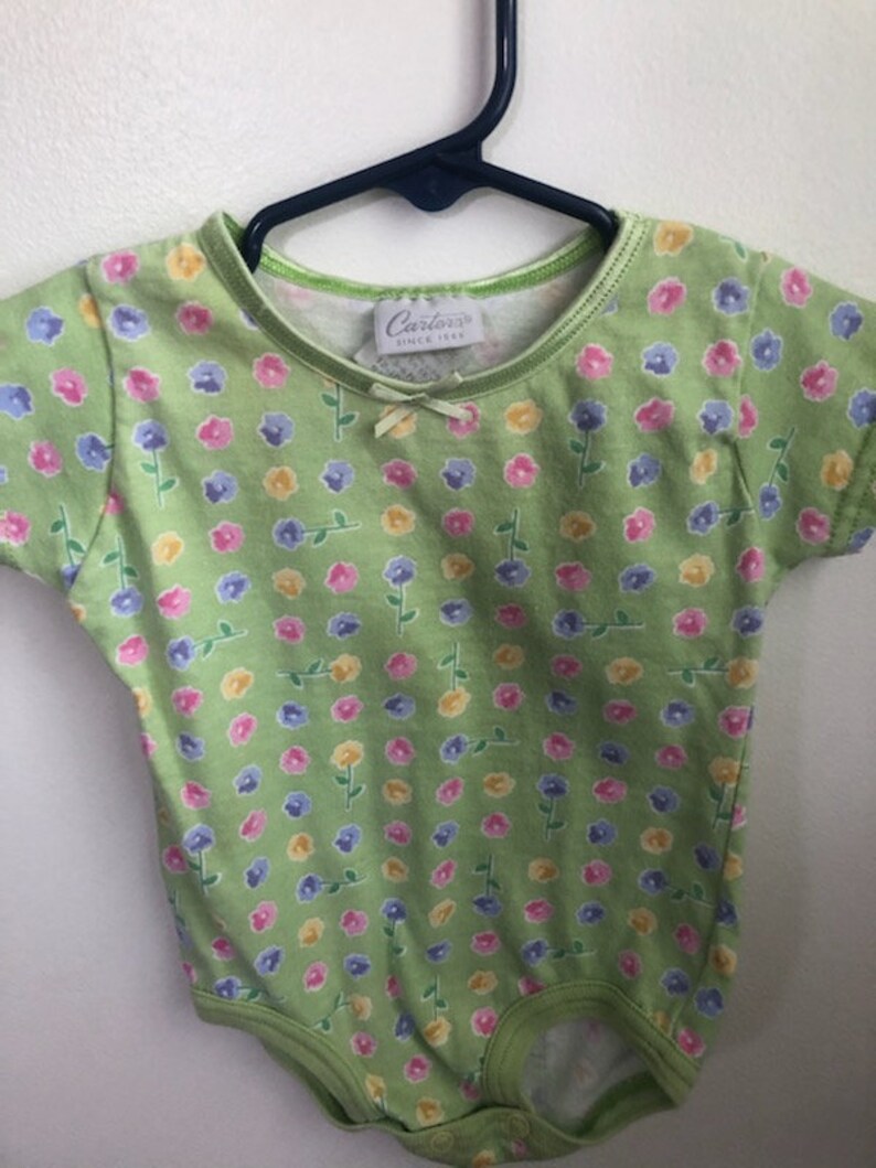 May include: A green baby onesie with a floral print. The onesie has a white tag with the text "Carter's Since 1865".
