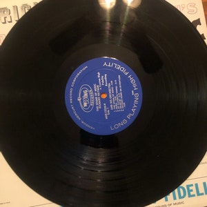 K&ouml;nnte beinhalten: Eine schwarze Schallplatte mit einem blauen Etikett, auf dem "Long Playing High Fidelity" und "Mercury Records Corporation" steht. Die Schallplatte ist mit "MGW 12228 - Richard Hayman and His Orchestra - The Sound of Music" beschriftet.