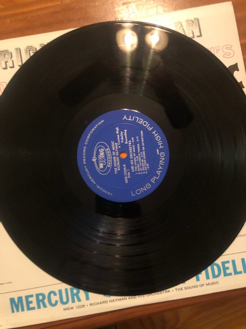 K&ouml;nnte beinhalten: Eine schwarze Schallplatte mit einem blauen Etikett, auf dem "Long Playing High Fidelity" und "Mercury Records Corporation" steht. Die Schallplatte ist mit "MGW 12228 - Richard Hayman and His Orchestra - The Sound of Music" beschriftet.