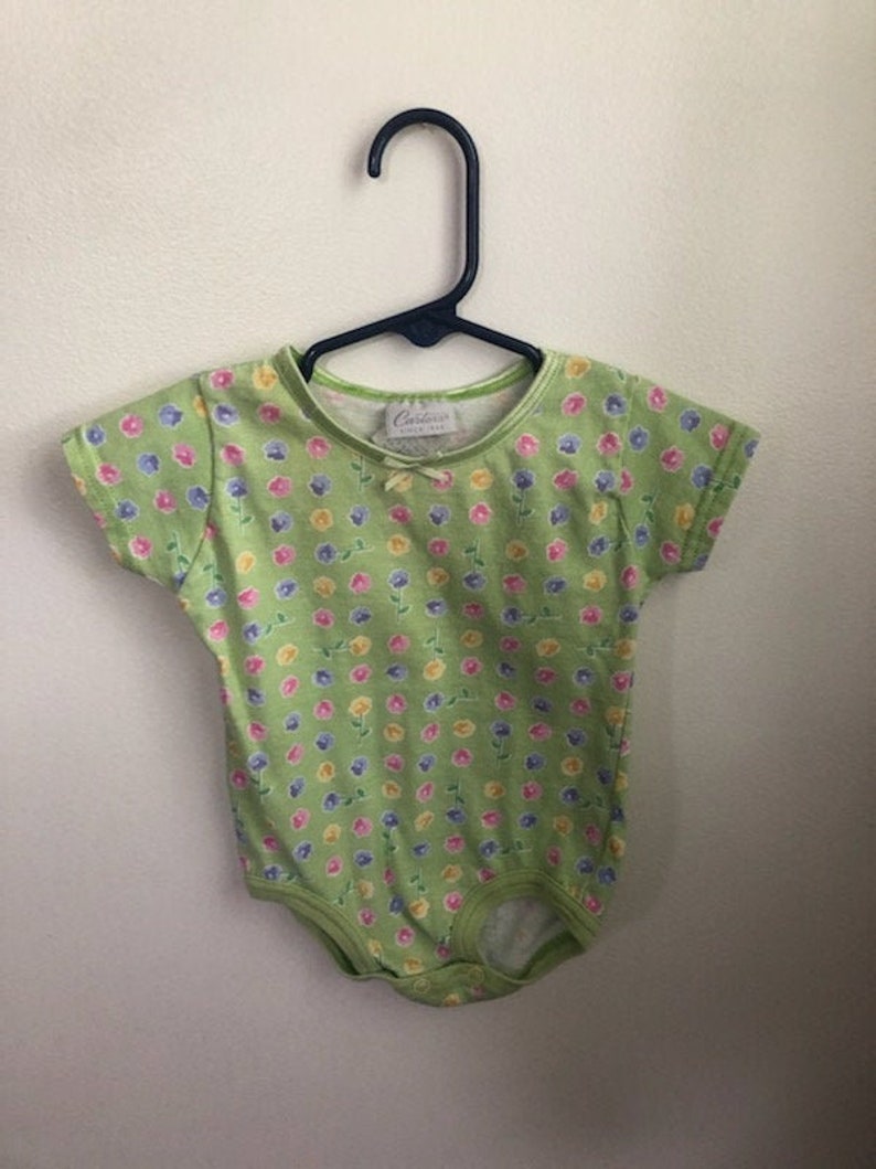 May include: A green baby onesie with a floral print. The onesie has a small white tag with the text "Carter's" on it.