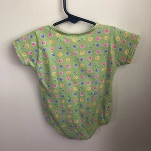 May include: A green short-sleeved bodysuit with a floral print featuring pink, yellow, and blue flowers.