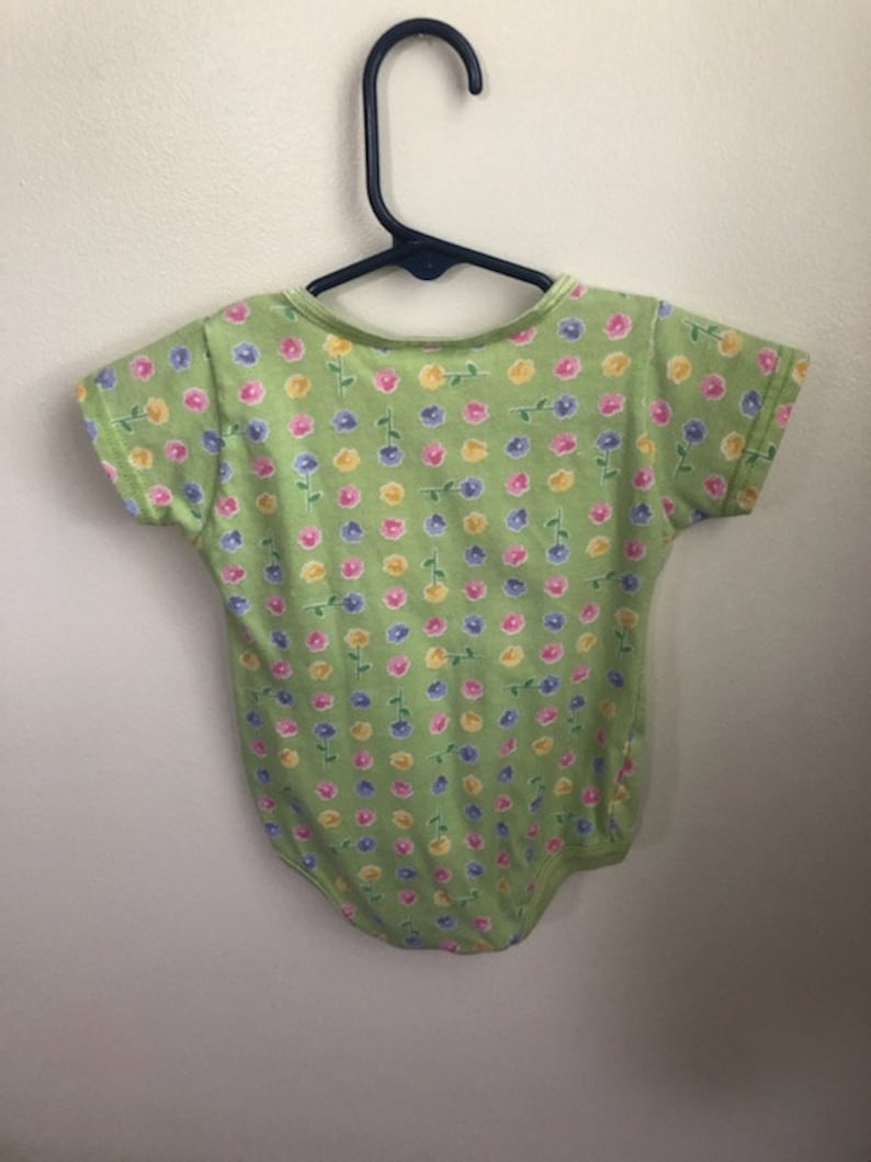 May include: A green short-sleeved bodysuit with a floral print featuring pink, yellow, and blue flowers.