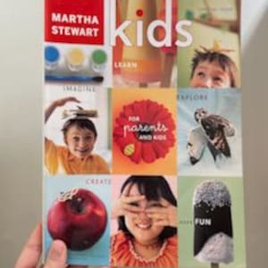May include: A person holding a copy of "Martha Stewart Kids" magazine. The cover features a collage of images, including paint, children, and the words "Imagine," "Learn," "Explore," "Create," and "Have Fun."