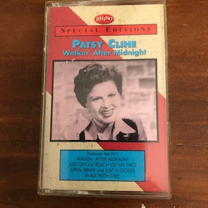May include: A red, white, and blue cassette tape with a picture of Patsy Cline on the front. The text on the tape reads "Rhino Special Editions Patsy Cline Walkin' After Midnight". The back of the tape lists the songs included: "Walkin' After Midnight", "Just Out of Reach (Of My Two Open Arms)", and "Just a Closer Walk with Thee".