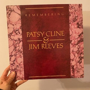 May include: A red vinyl record album with a marbled pink and black design. The album title is "Remembering Patsy Cline & Jim Reeves".