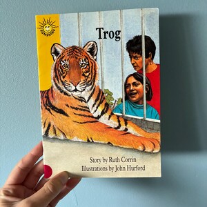 May include: A paperback book titled Trog from the Sunshine series. The cover features an illustration of a tiger lying down behind bars, with two people looking on. The text reads Story by Ruth Corrin and Illustrations by John Hurford.