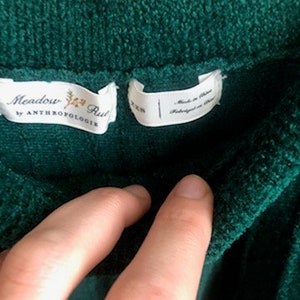 Puede incluir: Un su&eacute;ter verde oscuro, suave y peludo con una etiqueta blanca que dice "Meadow Rue by Anthropologie".