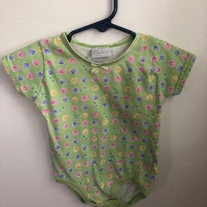 May include: A green baby onesie with a floral print. The onesie has a small bow on the front and says "Carter's Baby" on the tag.