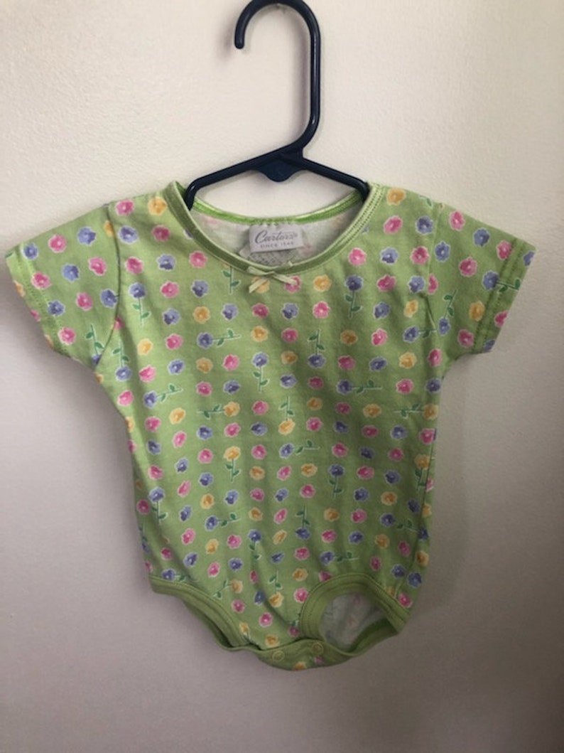 May include: A green baby onesie with a floral print. The onesie has a small bow on the front and says "Carter's Baby" on the tag.