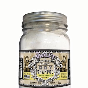 May include: A glass jar with a silver lid containing a white powder. The label reads "The Violet Apawthecary Fairy Dry Shampoo Lemon Verbena Scent" and "Refreshes Fur Simple To Use". The jar is 12 ounces.